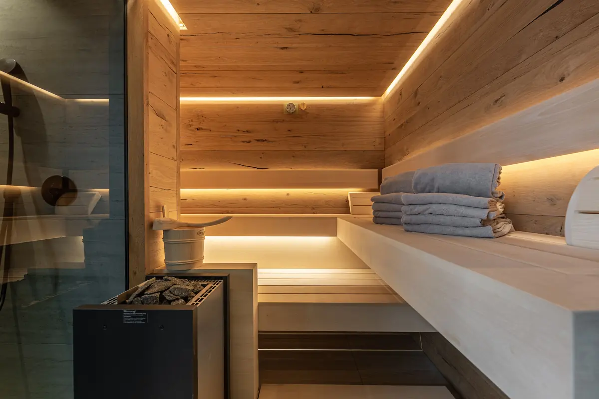 Sauna mit hellen Holzbänken, Ofen, Handtüchern und warmem Licht